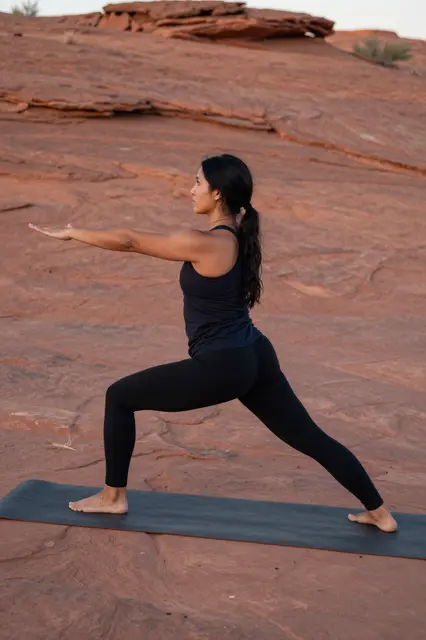 Side view of a woman practicing yoga on a mat over red desert rock at dawn