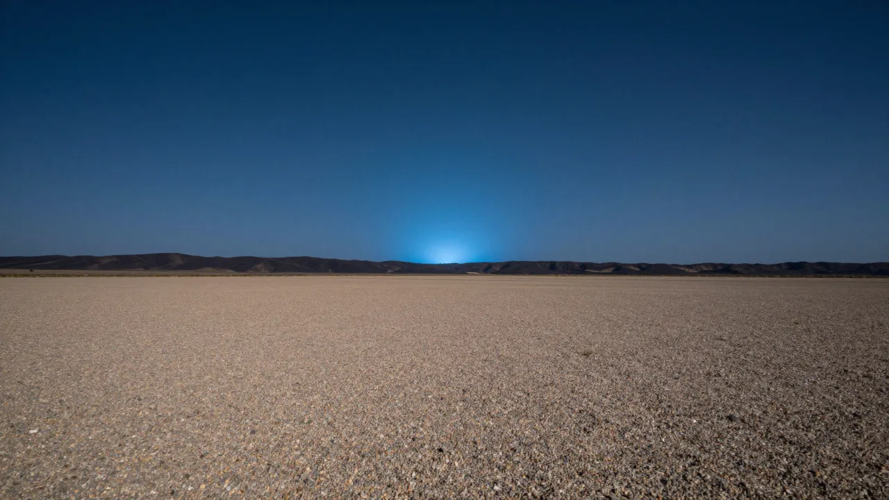 Vast gravel desert plain stretches toward distant dark hills under a deepening twilight night sky