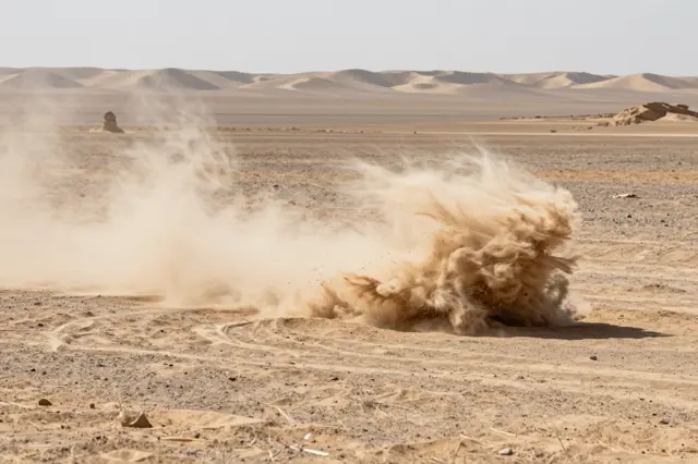 A swirling dust devil rises from arid desert flatland under bright afternoon sun with distant sand dunes on the horizon