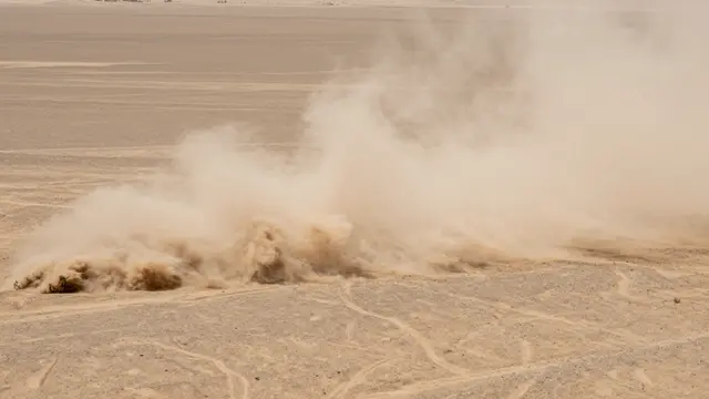 A thick churning dust storm billows across a flat arid desert plain with faint tire tracks