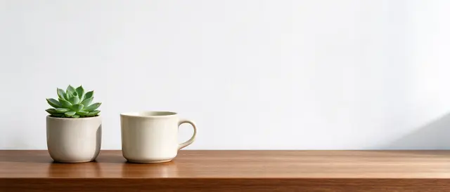 Potted succulent and ceramic mug sit on a wooden desk against an empty white wall