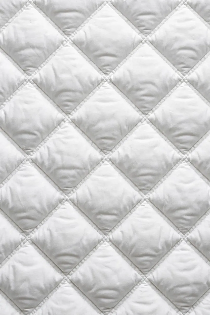 Full frame close up of puffy diamond-quilted white padded fabric with even flat lighting