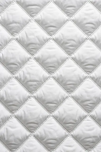 Full frame close up of puffy diamond-quilted white padded fabric with even flat lighting