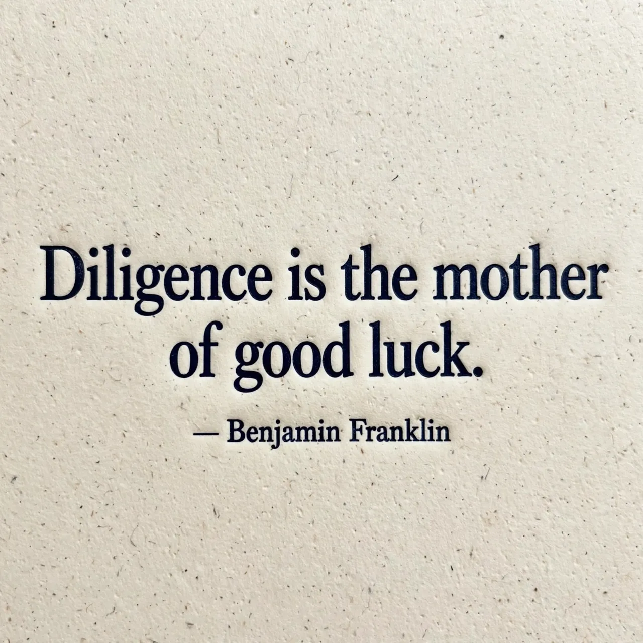 Deep navy debossed letterpress quote on textured cream cotton paper reading "Diligence is the mother of good luck.