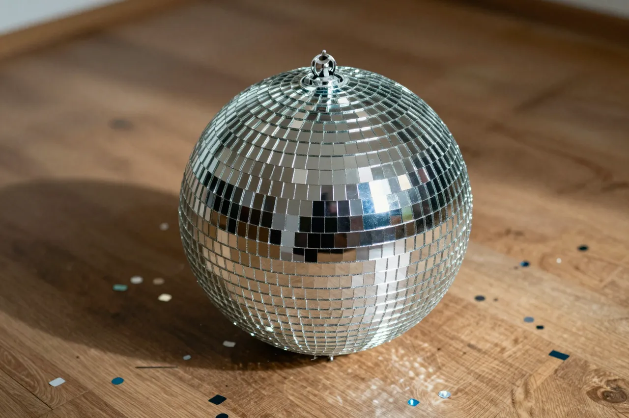 A mirrored disco ball rests on a wooden floor surrounded by scattered colorful confetti.
