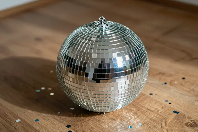 A mirrored disco ball rests on a wooden floor surrounded by scattered colorful confetti.