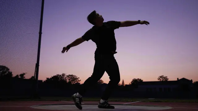 Silhouette of an adult discus thrower in motion on a track and field circle against a gradient dusk sky