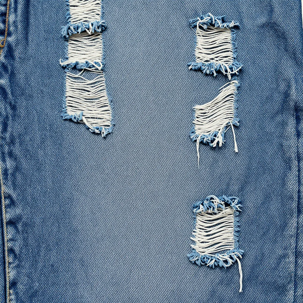 Faded blue distressed denim fabric with frayed ripped details fills the full frame