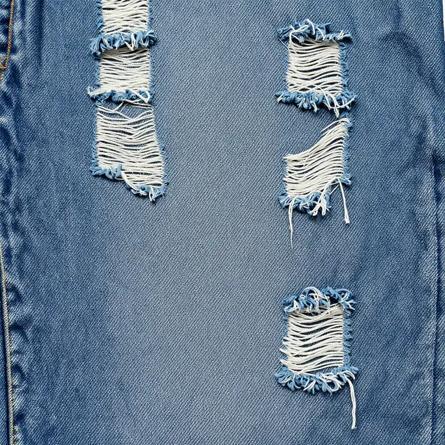 Faded blue distressed denim fabric with frayed ripped details fills the full frame