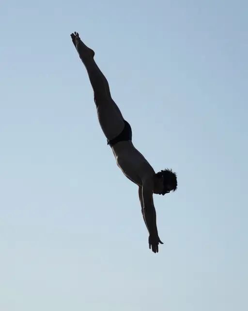 Silhouette of an adult diver in a diving pose against a pale clear blue sky