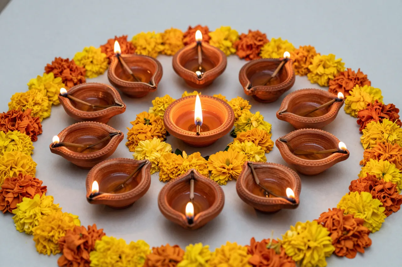 Lit clay diya lamps arranged in a circle framed by yellow and orange flower rangoli for Diwali