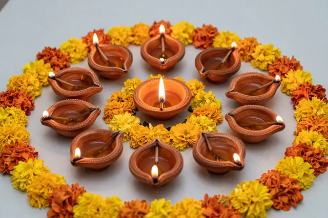 Lit clay diya lamps arranged in a circle framed by yellow and orange flower rangoli for Diwali