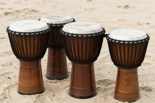 Four wooden djembe drums arranged in a row resting on light beach sand