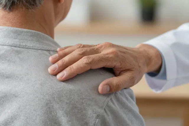 Close-up of a doctor's hand resting gently on a senior patient's shoulder in a clinical setting