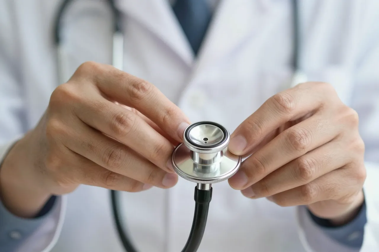 Close-up of a doctor's hands holding the chest piece of a stethoscope, with a blurred lab coat in the background.