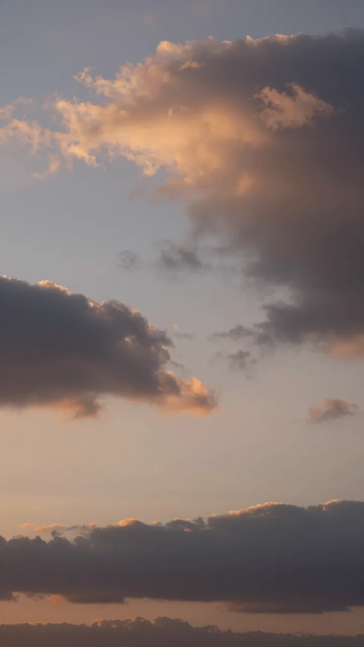 Vertical view of a sunset sky filled with dramatic clouds tinted warm orange and soft blue.
