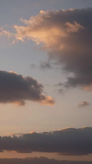 Vertical view of a sunset sky filled with dramatic clouds tinted warm orange and soft blue.
