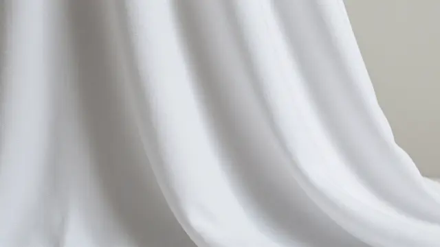 Soft draped white fabric with gentle folds catches light, with empty neutral space to the right of the frame