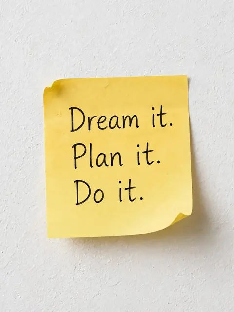 Yellow sticky note with handwritten "Dream it. Plan it. Do it." stuck to a textured white wall