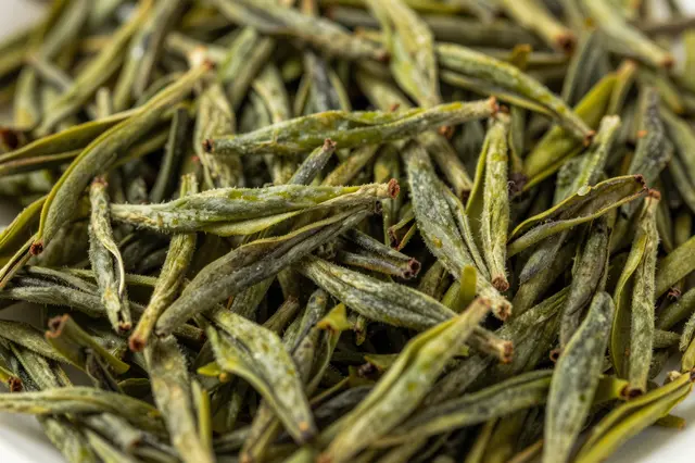 Close-up full-frame view of loose dried green tea leaves with fine fuzzy texture and varying green hues.