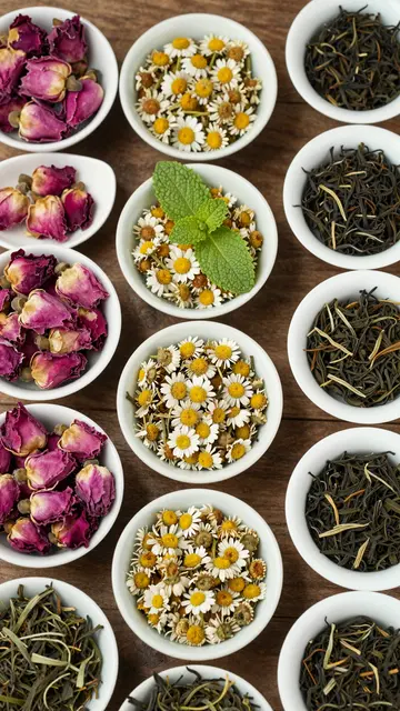 Top-down flat lay of small white ceramic bowls holding dried tea, rose petals, chamomile, and mint on a rustic wooden table.