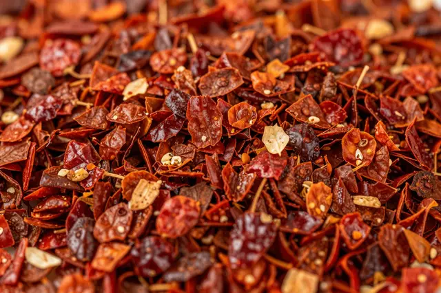 A tight full-frame close-up of textured dried red chili flakes with visible seeds and fragmented pieces.