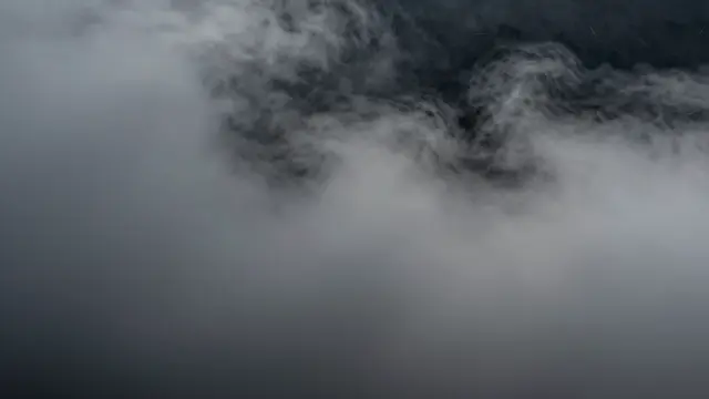 Wispy thick gray fog drifts across a deep muted dark background