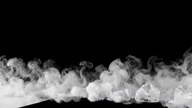 Wispy white dry ice fog and ice chunks creep along the bottom edge of a solid pure black background