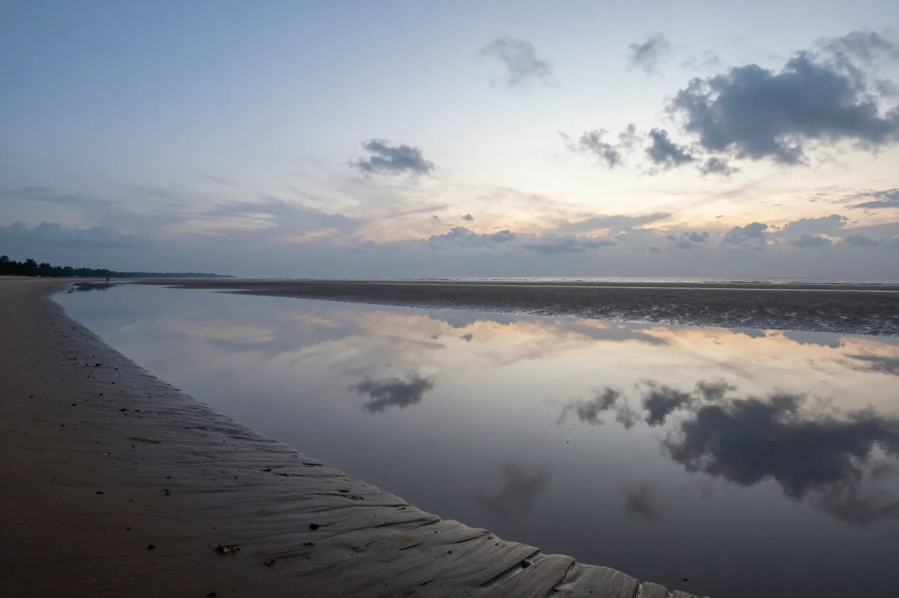 Calm shallow tidal lagoon reflects the pastel dusk sky over a wide sandy beach