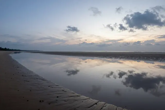 Calm shallow tidal lagoon reflects the pastel dusk sky over a wide sandy beach