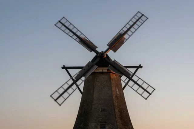 Low angle view of an old brick windmill with softly blurred spinning sails against a pale dusk sky