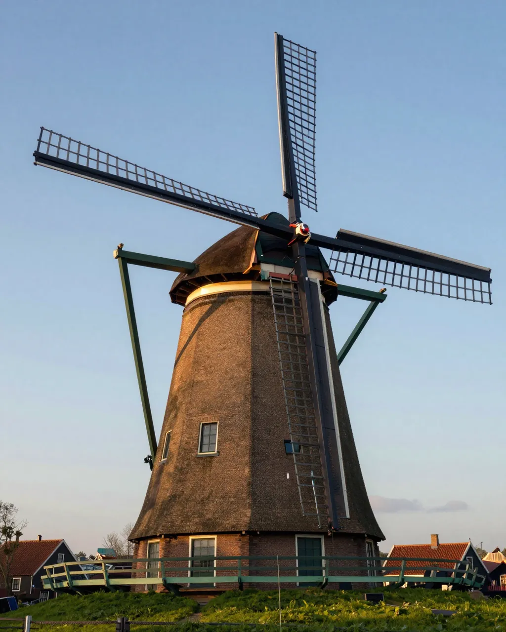A tall traditional brick Dutch windmill stands on grass with village houses at soft dusk