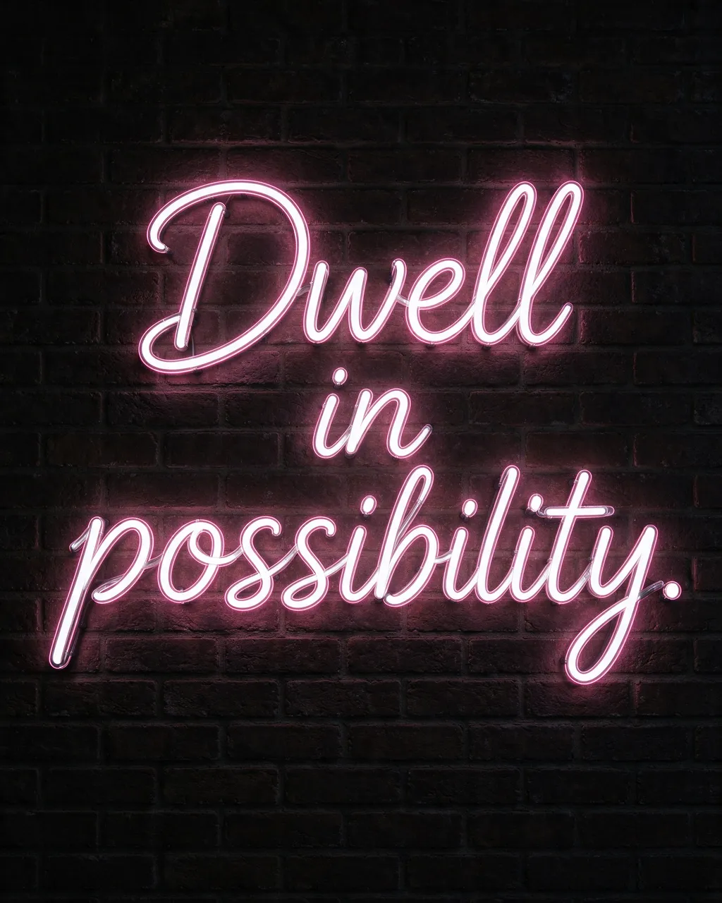 Glowing white neon sign with soft pink halo displaying "Dwell in possibility." mounted on a dark brick wall at night