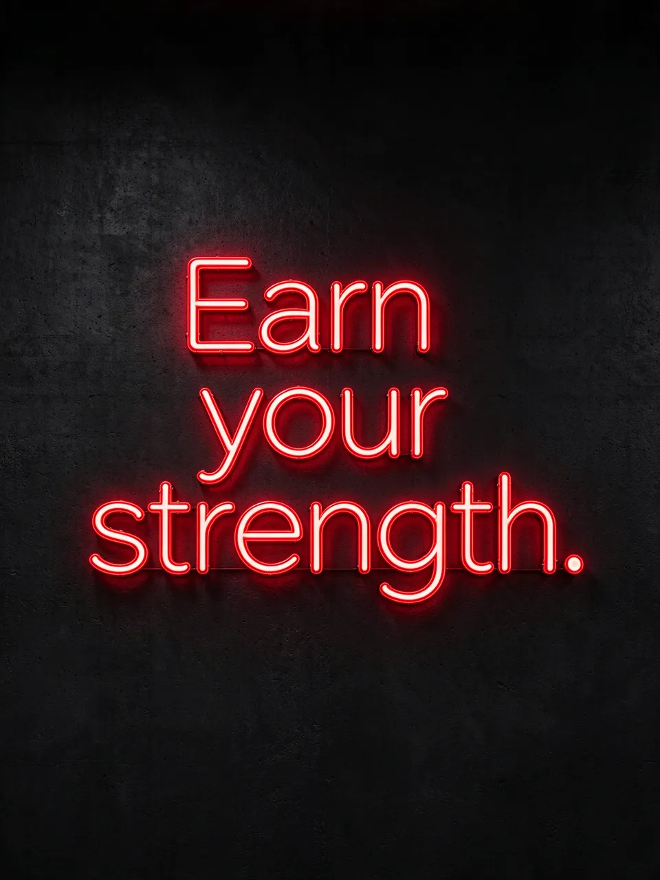 Glowing red neon sign reading "Earn your strength." mounted on a dark textured concrete wall