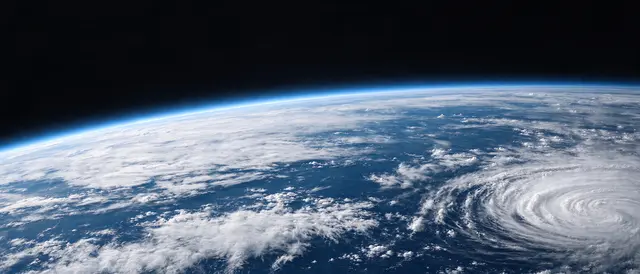 Curved edge of sunlit Earth showing swirling clouds over deep blue ocean set against the black of outer space