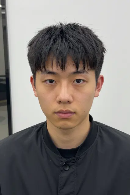 Headshot portrait of a late twenties East Asian man with a two-block haircut wearing a black jacket