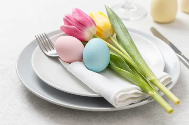 A neatly arranged Easter place setting holds pastel eggs, fresh tulips, and silver flatware on linen.
