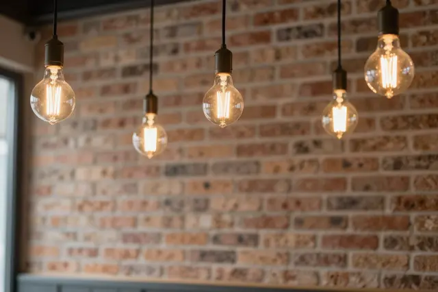 Five hanging lit filament pendant bulbs in front of a textured exposed brick restaurant wall