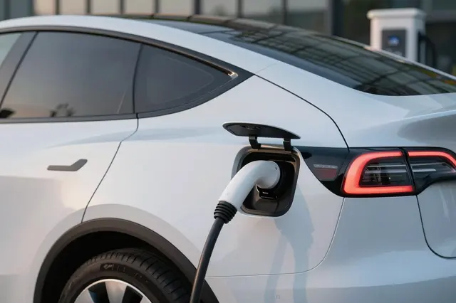 A close-up side view of a white unbranded electric car plugged in to charge at a station during dusk