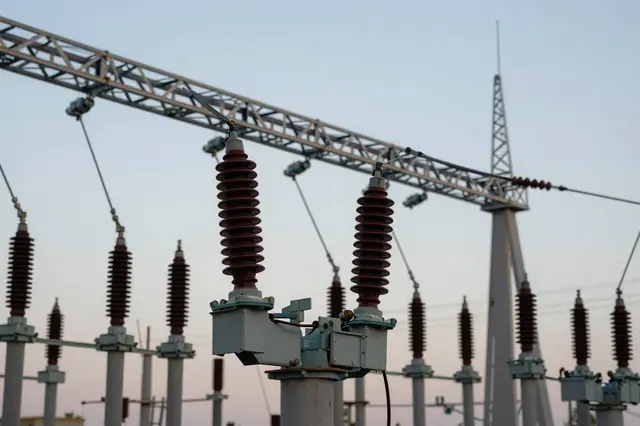 High voltage insulators and substation structural gantries stand against a pale dusk sky