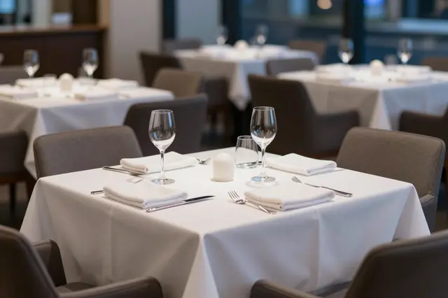 Set restaurant tables with white tablecloths sit ready for service at dusk