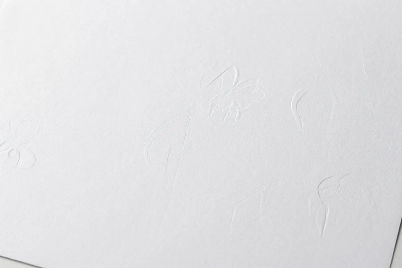 Close-up view of white paper with subtle raised floral embossed relief details