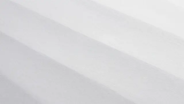 Full frame close-up of blind embossed white paper with soft raised waves lit by raking light