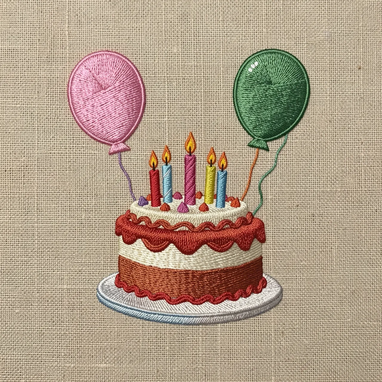 Stitched embroidery artwork of a birthday cake with candles and two balloons on natural linen fabric