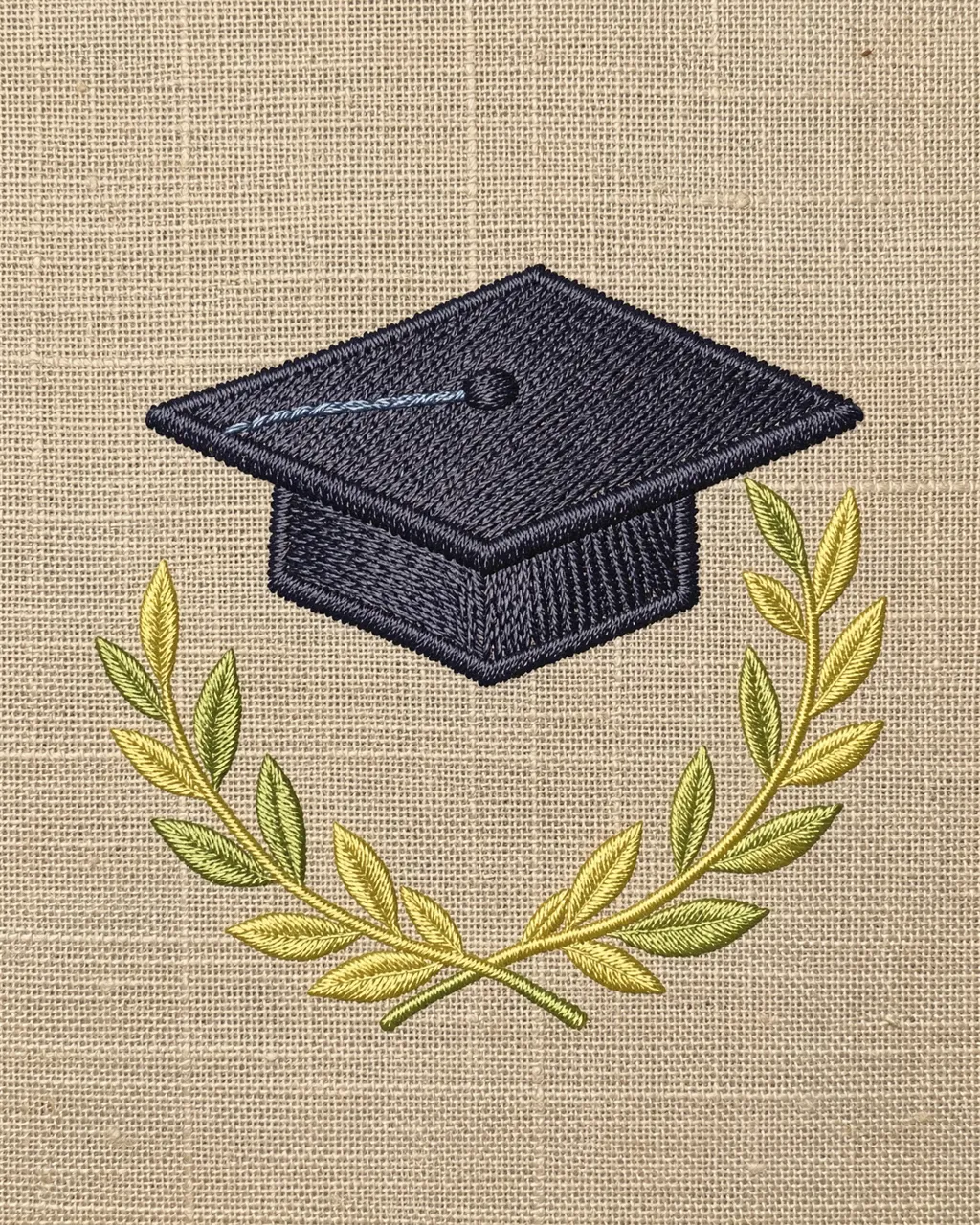 Stitched embroidery of a graduation cap above a laurel wreath on natural linen fabric