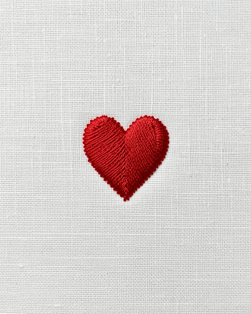 A stitched red heart centered on a plain white linen fabric background