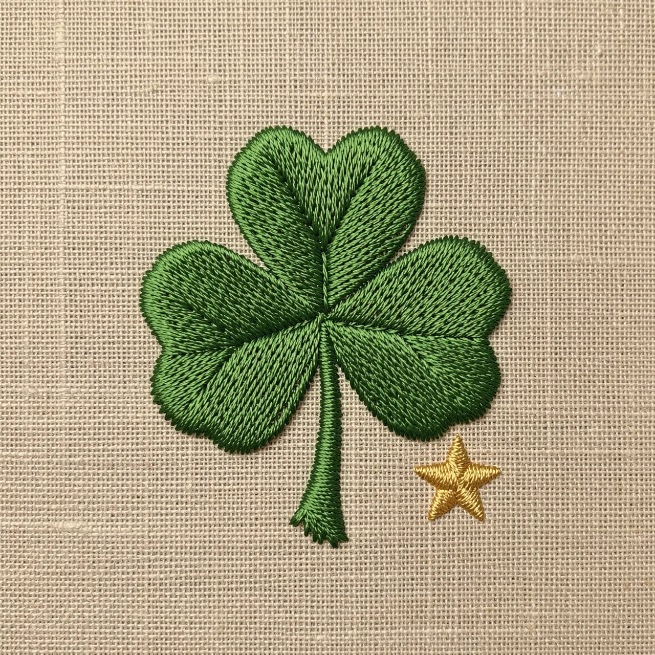 Stitched green shamrock and small gold star rest on a natural linen fabric background