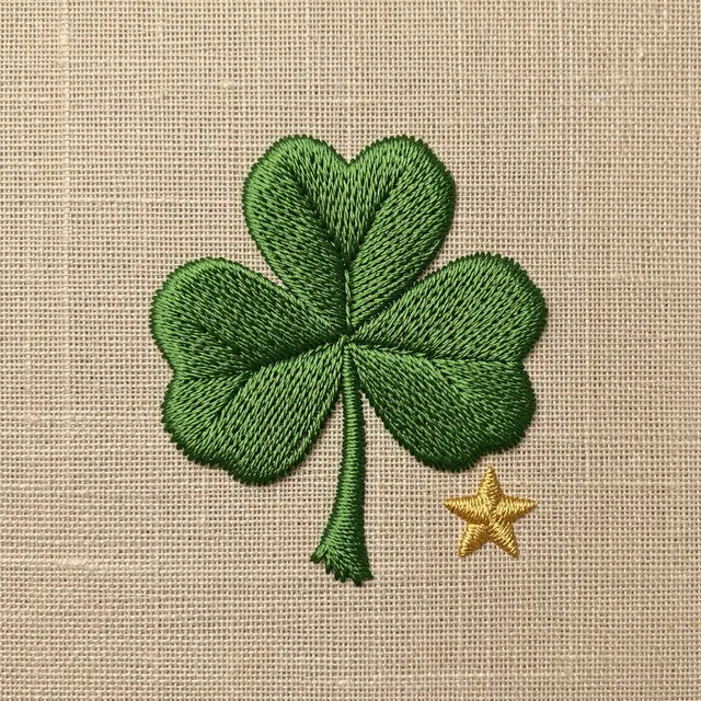 Stitched green shamrock and small gold star rest on a natural linen fabric background