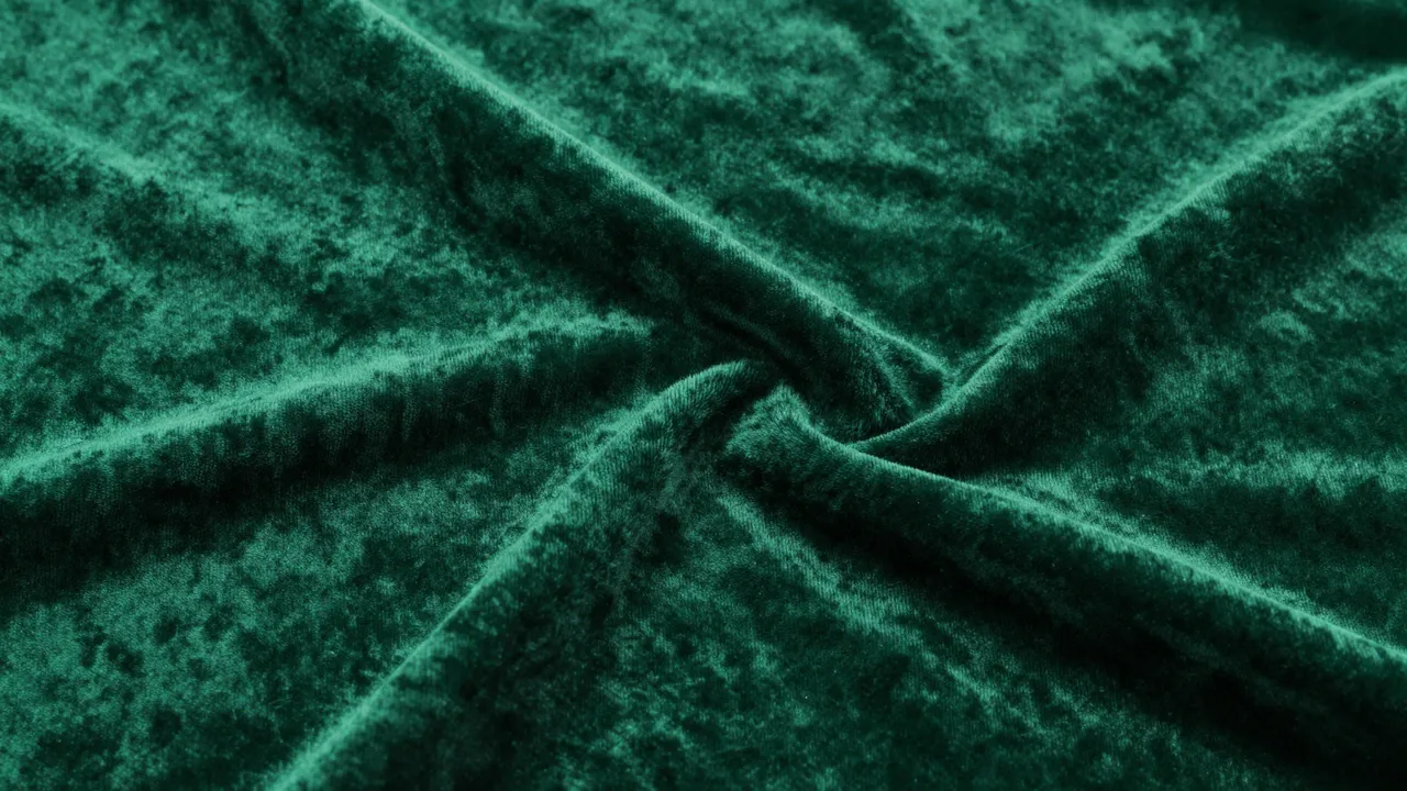 Close-up full frame of soft twisted emerald green velvet fabric with natural folds and sheen