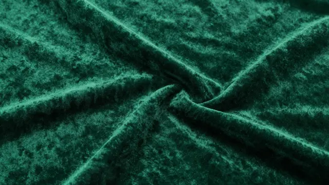 Close-up full frame of soft twisted emerald green velvet fabric with natural folds and sheen